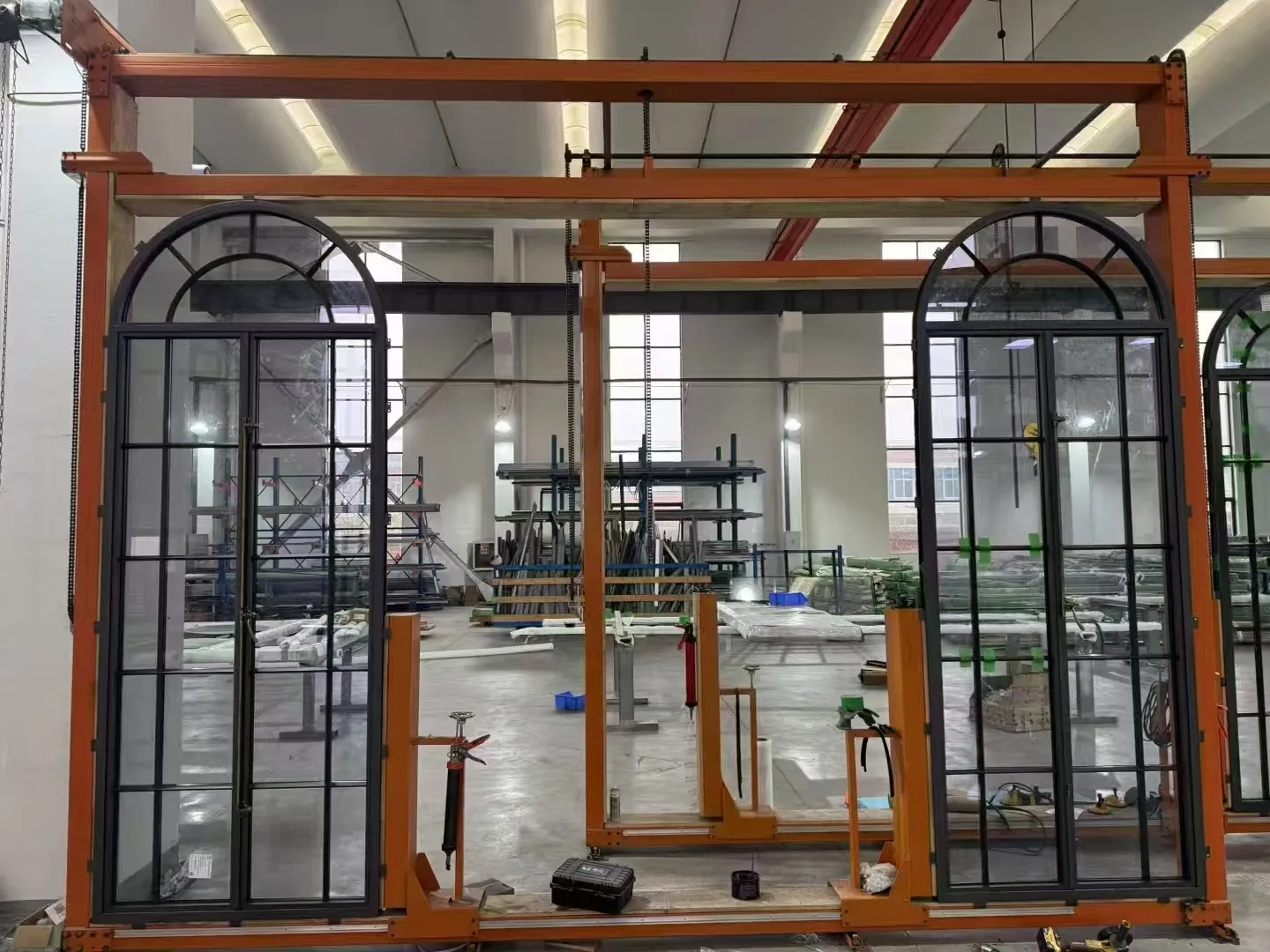 Arched steel window units held on a painting line gantry, each with a fanlight of radiating glazing bars above a multi-pane lower grid. Arched heads and true divided lites like these are the details heritage projects are judged on.