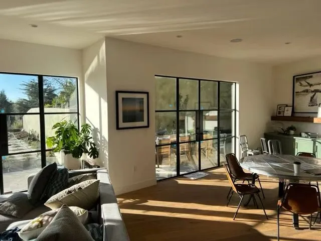 A living room fitted with slim black steel-framed glazed doors and a matching internal window. The narrow frames and regular grid let daylight and the garden read as part of the room rather than a view framed by it.